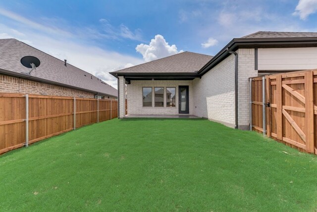 back of house with brick siding, a fenced backyard, and a lawn