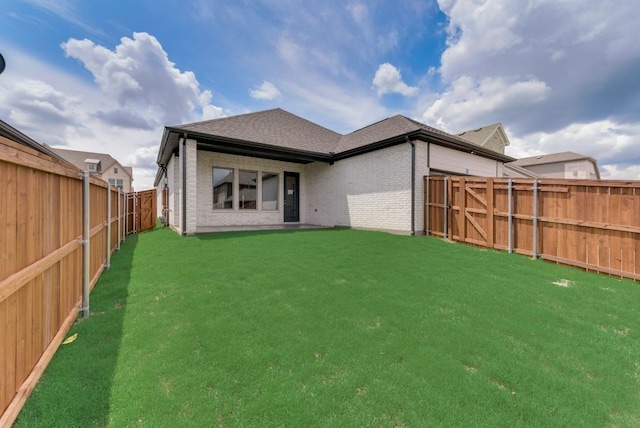 rear view of house featuring brick siding, a lawn, a shingled roof, and a fenced backyard