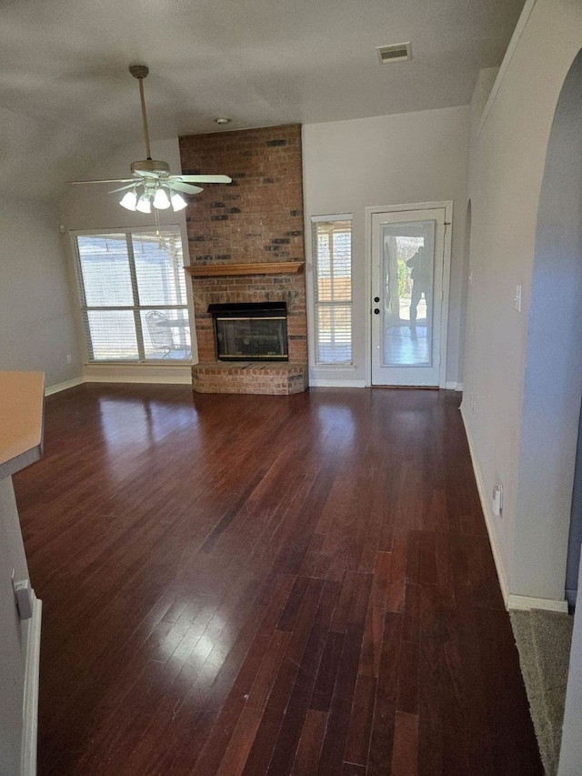 unfurnished living room featuring a fireplace, arched walkways, visible vents, and a wealth of natural light