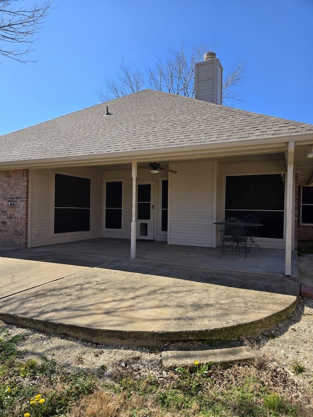 back of house featuring a ceiling fan, a shingled roof, brick siding, a chimney, and a patio area