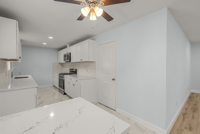 kitchen featuring baseboards, decorative backsplash, stainless steel appliances, a ceiling fan, and a sink