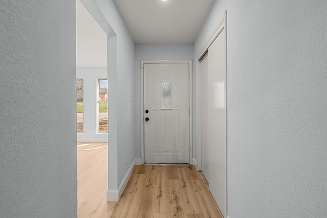 doorway to outside featuring baseboards, light wood-style floors, and a textured wall