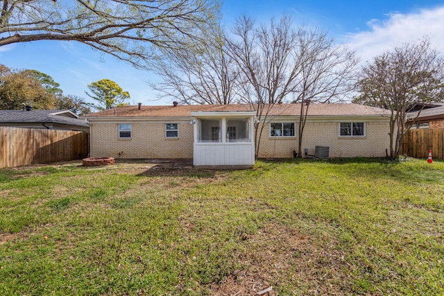 back of property with a fenced backyard, central AC, a fire pit, a lawn, and brick siding