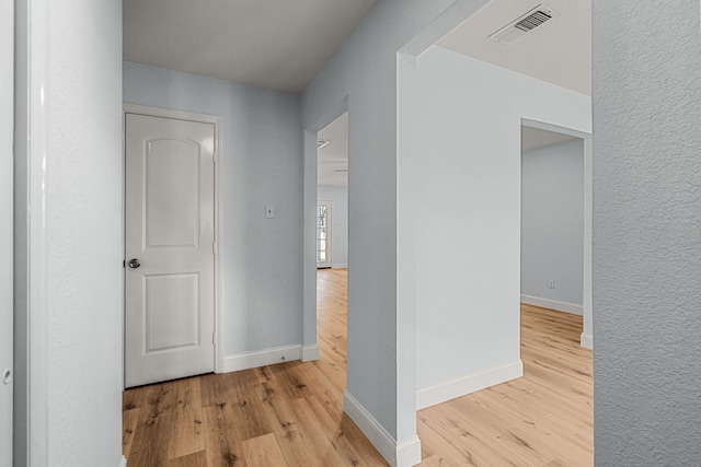 hall with visible vents, baseboards, and wood finished floors