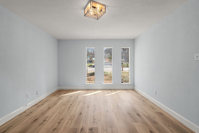 unfurnished room with wood finished floors, baseboards, a textured wall, and a textured ceiling