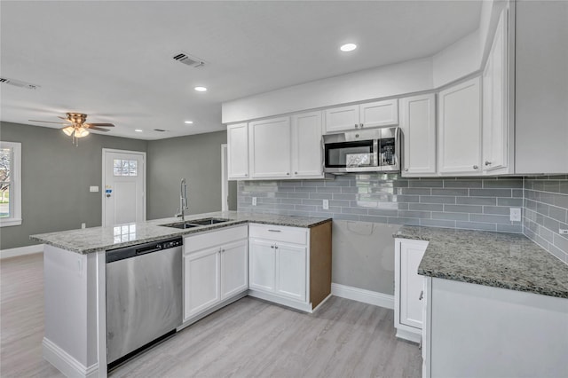 kitchen featuring visible vents, light stone counters, a peninsula, stainless steel appliances, and a sink