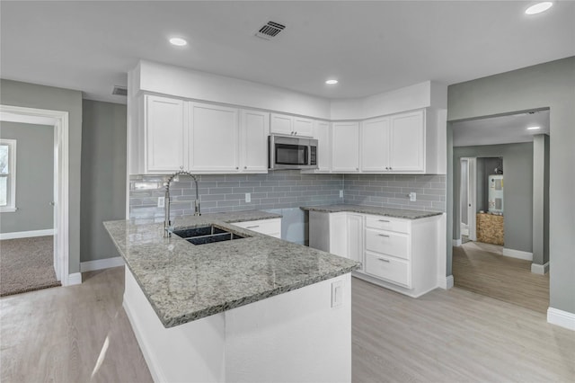 kitchen with stainless steel microwave, white cabinets, light stone countertops, and a sink