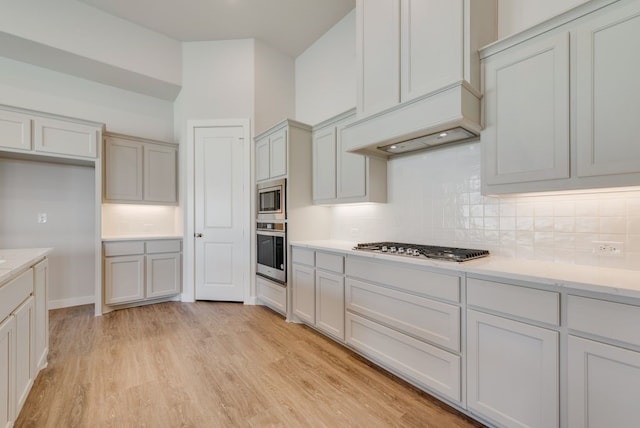 kitchen featuring custom exhaust hood, decorative backsplash, appliances with stainless steel finishes, and light wood-type flooring