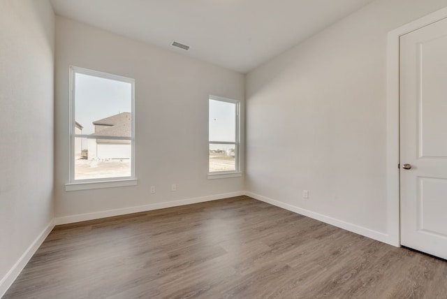 empty room featuring wood finished floors, visible vents, a wealth of natural light, and baseboards