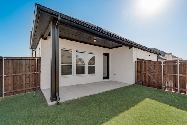 back of property with brick siding, a patio area, a lawn, and fence