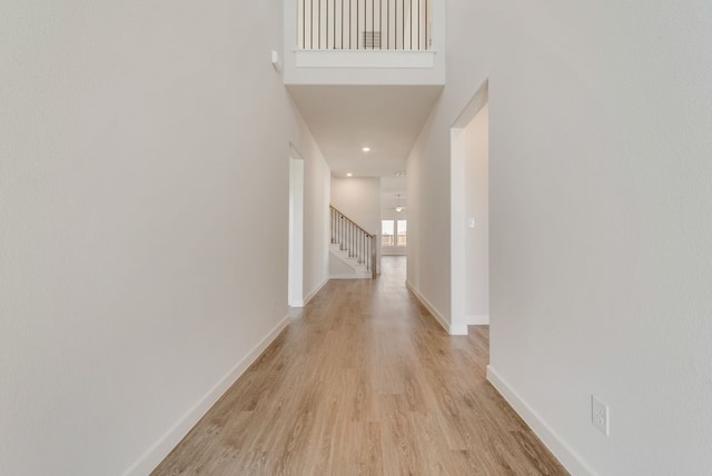 corridor with baseboards, stairs, light wood-style floors, and a towering ceiling