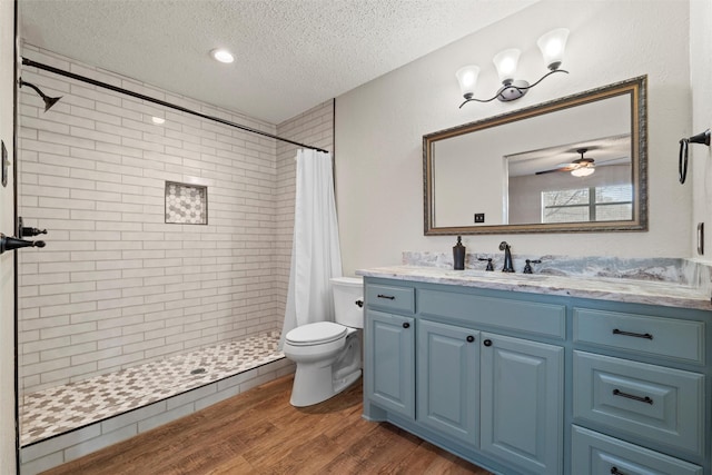 bathroom with vanity, wood finished floors, tiled shower, a textured ceiling, and toilet