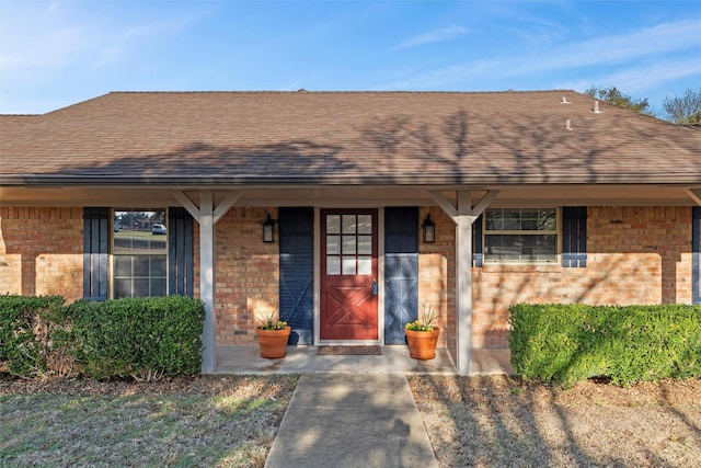 property entrance with a porch, brick siding, and roof with shingles