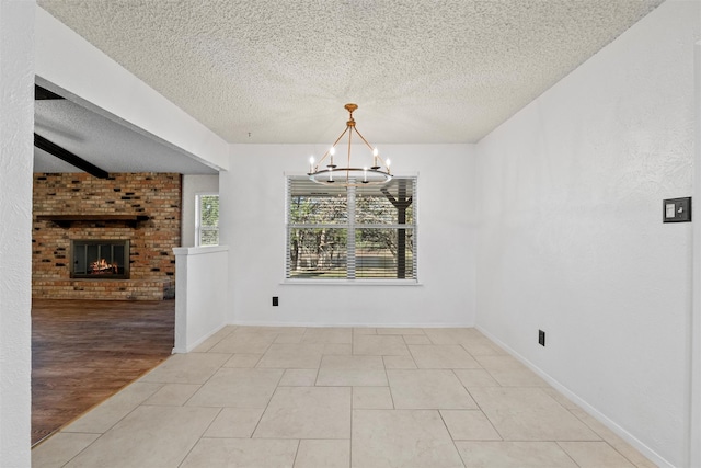 unfurnished dining area with a chandelier, light tile patterned floors, beam ceiling, a fireplace, and a textured ceiling