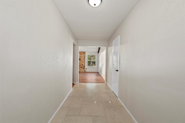 corridor featuring light tile patterned flooring, a textured ceiling, baseboards, and a textured wall