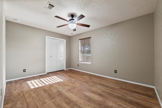 unfurnished bedroom featuring visible vents, a textured ceiling, wood finished floors, a closet, and baseboards