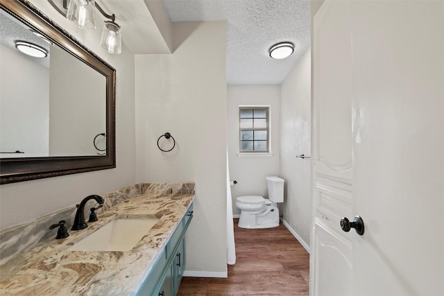 bathroom with baseboards, toilet, vanity, wood finished floors, and a textured ceiling