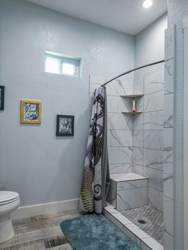 full bathroom featuring toilet, baseboards, a stall shower, and a textured wall