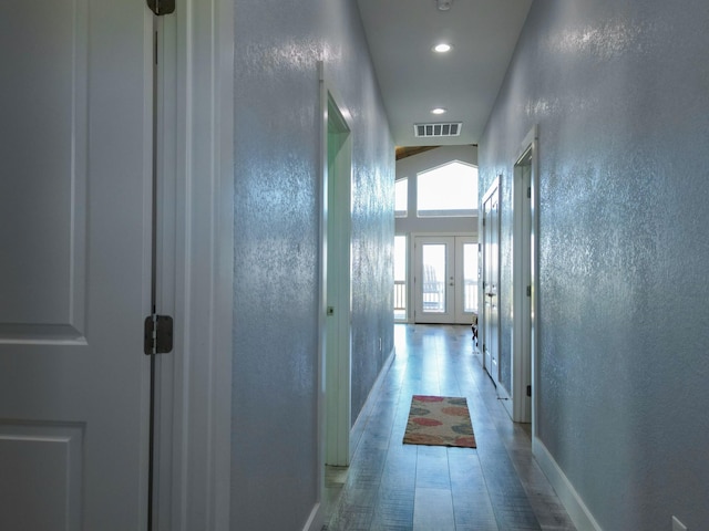 hall featuring light wood-type flooring, visible vents, baseboards, and a textured wall