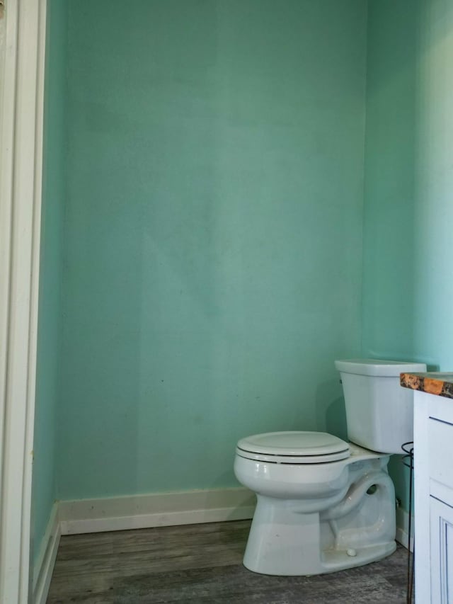 half bathroom with toilet, vanity, baseboards, and wood finished floors