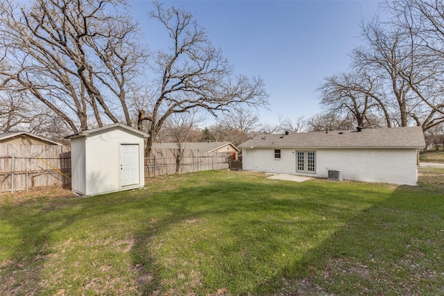 view of yard featuring central AC, french doors, a fenced backyard, an outbuilding, and a storage unit