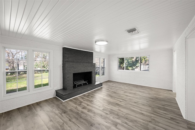 unfurnished living room featuring visible vents, wood finished floors, brick wall, a fireplace, and wood ceiling