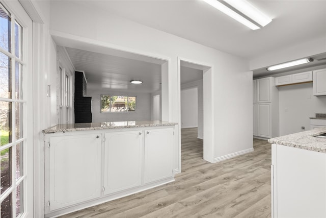 kitchen with light stone counters, white cabinets, baseboards, and light wood-style floors