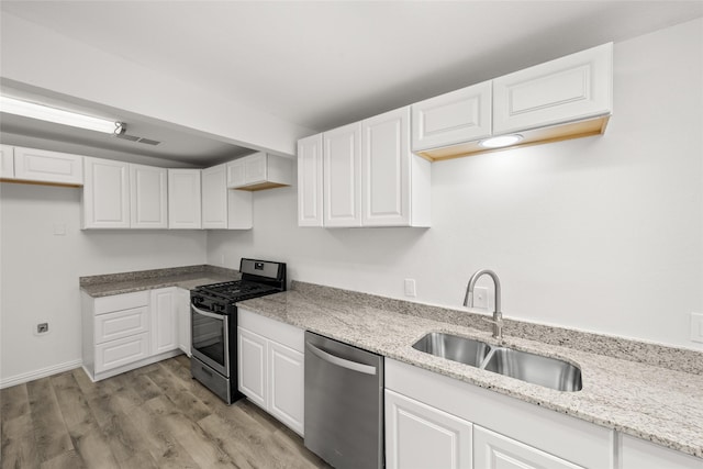 kitchen featuring light stone counters, light wood-style flooring, a sink, white cabinets, and appliances with stainless steel finishes