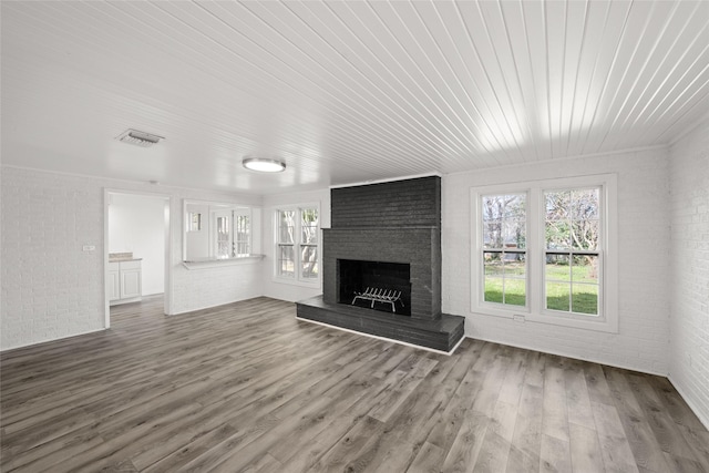 unfurnished living room featuring a fireplace, wood finished floors, visible vents, and brick wall