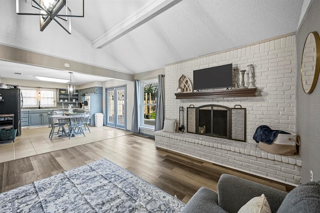 living area with high vaulted ceiling, beam ceiling, a fireplace, a textured ceiling, and light wood-type flooring