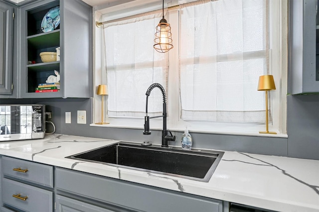 kitchen with decorative light fixtures, gray cabinetry, open shelves, and a sink