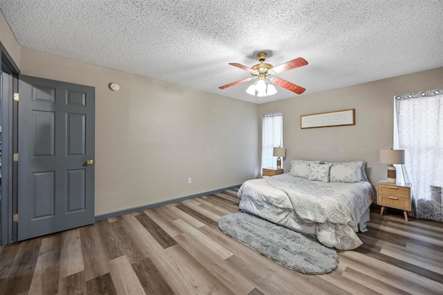 bedroom featuring baseboards, a textured ceiling, wood finished floors, and a ceiling fan