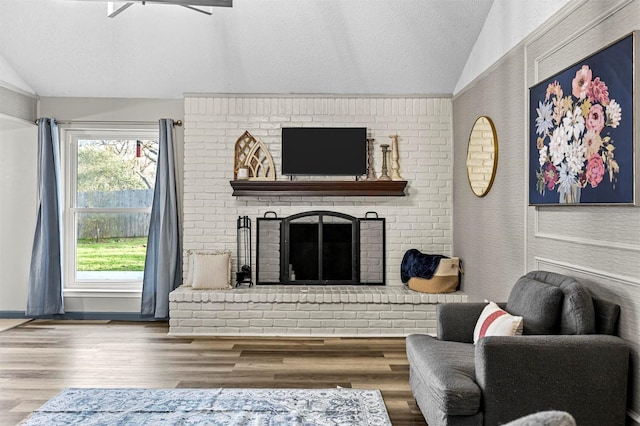 living room with a textured ceiling, wood finished floors, a brick fireplace, ceiling fan, and vaulted ceiling