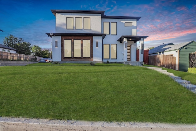 back of property at dusk with fence and a lawn