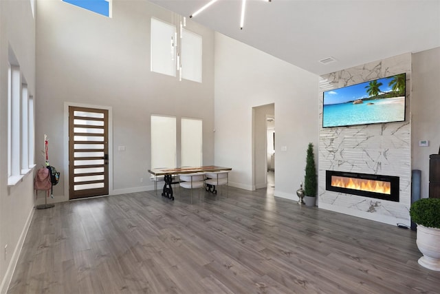 unfurnished living room with wood finished floors, visible vents, baseboards, a high ceiling, and a high end fireplace