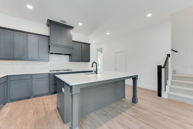 kitchen with a center island with sink, visible vents, light countertops, custom range hood, and light wood-style floors