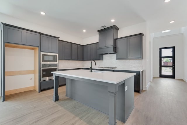 kitchen with built in microwave, an island with sink, custom range hood, stainless steel oven, and a sink