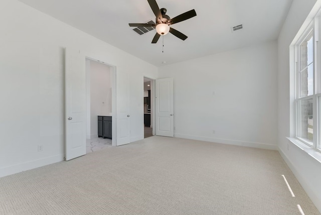 empty room with plenty of natural light, light colored carpet, visible vents, and a ceiling fan