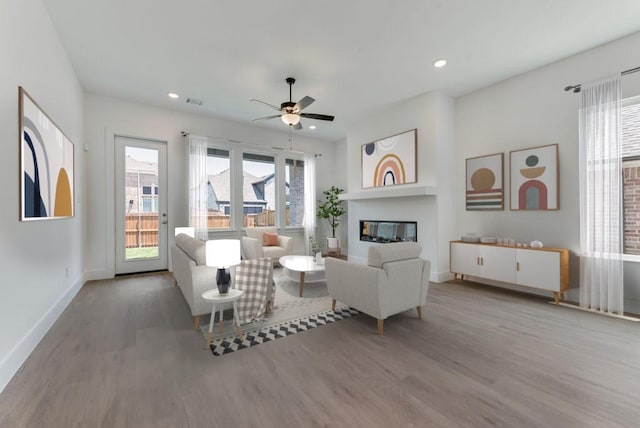 living room featuring a ceiling fan, a glass covered fireplace, wood finished floors, recessed lighting, and baseboards