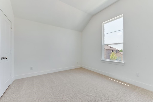 additional living space featuring vaulted ceiling, baseboards, and light carpet