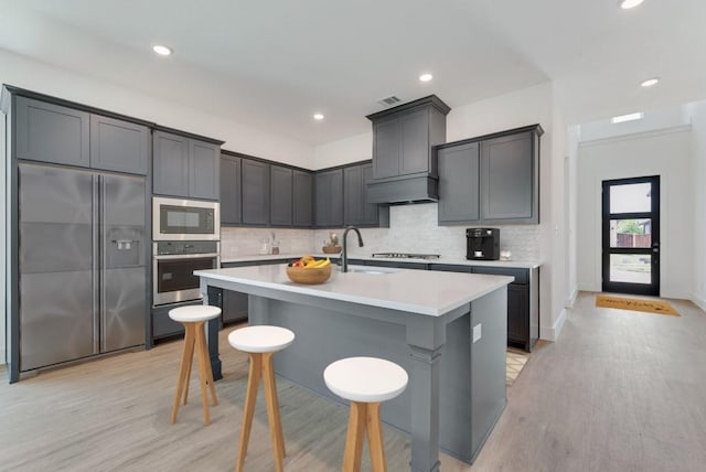 kitchen with premium range hood, a kitchen breakfast bar, tasteful backsplash, light countertops, and built in appliances