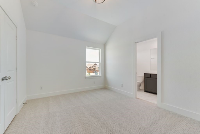 unfurnished bedroom with light carpet, baseboards, ensuite bath, and lofted ceiling