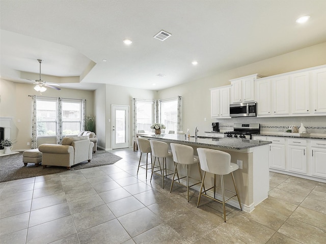 kitchen with a kitchen bar, visible vents, open floor plan, stainless steel appliances, and decorative backsplash