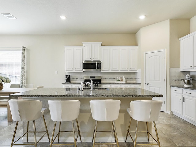 kitchen with visible vents, a kitchen bar, decorative backsplash, appliances with stainless steel finishes, and a kitchen island with sink