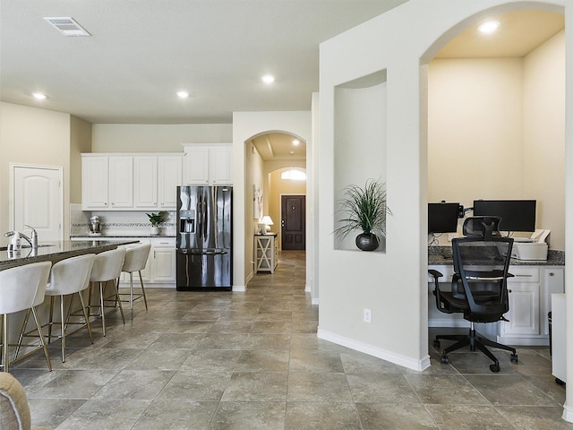 kitchen featuring visible vents, refrigerator with ice dispenser, a kitchen breakfast bar, arched walkways, and white cabinets