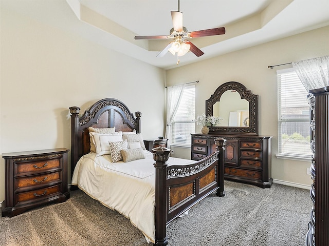 carpeted bedroom with baseboards, a raised ceiling, and a ceiling fan