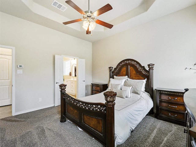 carpeted bedroom featuring baseboards, visible vents, ceiling fan, ensuite bathroom, and a raised ceiling