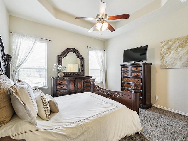 carpeted bedroom featuring a raised ceiling, baseboards, and ceiling fan