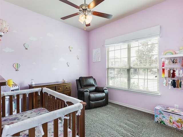 bedroom with a crib, a ceiling fan, baseboards, and carpet floors