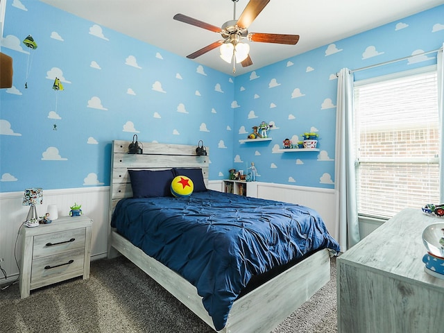 carpeted bedroom with wainscoting, wallpapered walls, and a ceiling fan